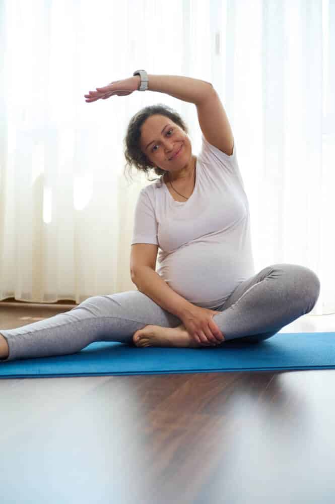 Smiling pregnant woman exercising on mat at home. Prenatal stretching exercises. Fitness. Pregnancy. Maternity lifestyle gym grossesse - Don Du Souffle