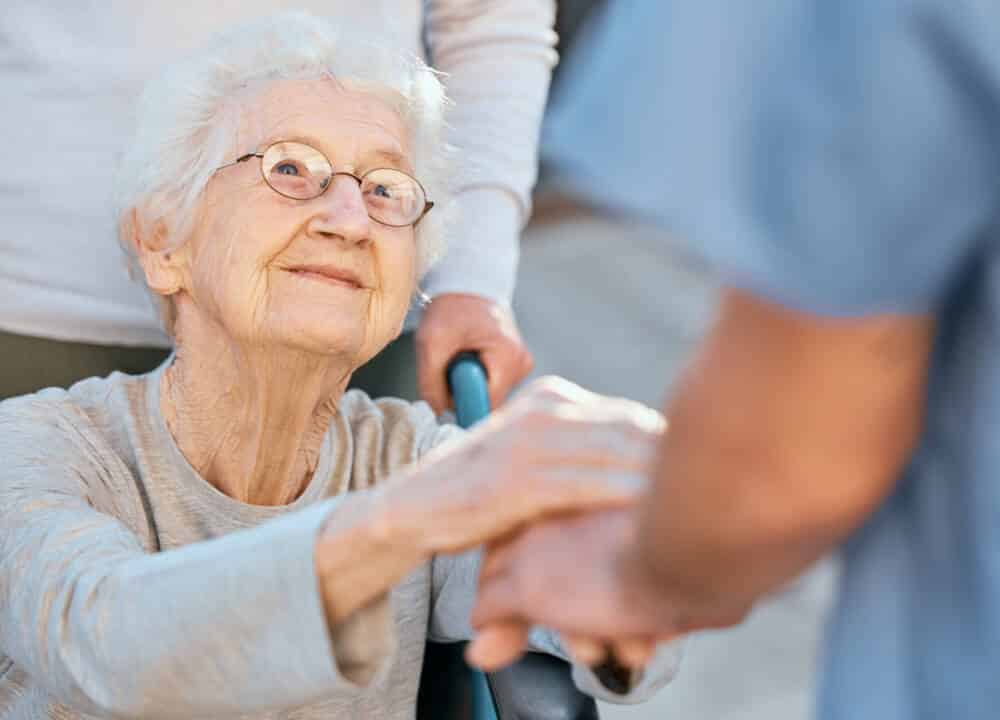 Holding hands, caregiver and senior woman in wheelchair for support outdoor in retirement home. Love, trust and healthcare nurse or medical wellness doctor for disability patient with kindness parkidanse - Don Du Souffle